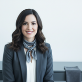 Portrait of Lauren Smith, a woman with dark hair, smiling confidently in a tailored charcoal blazer against a clean white bac